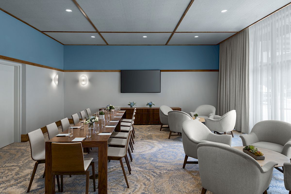 The image shows a modern conference room with a long table, chairs, a TV screen, and lounge seating; it has blue walls and patterned carpet.