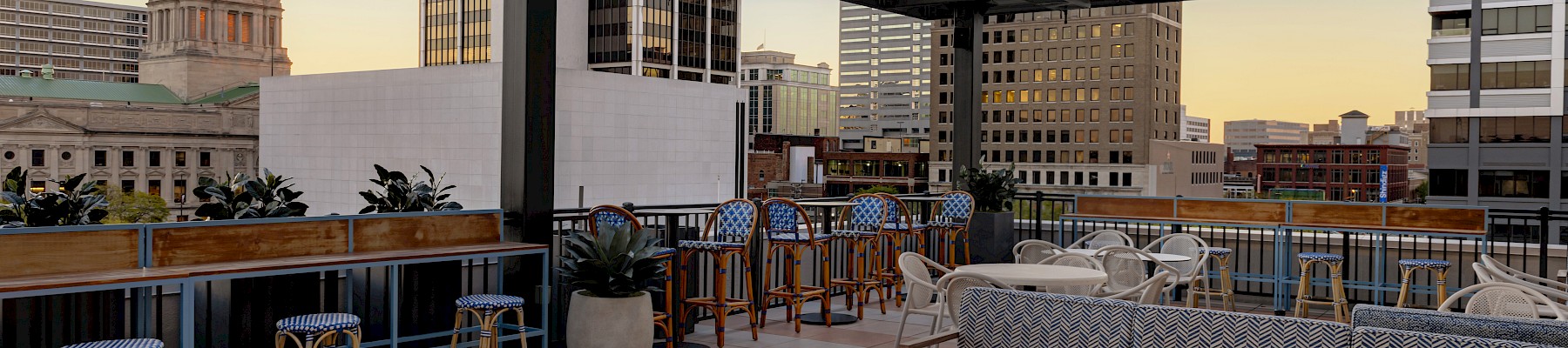 Rooftop lounge with sofas, fire pit, bar stools, and cityscape view. The area is open-air and stylish, perfect for social gatherings.