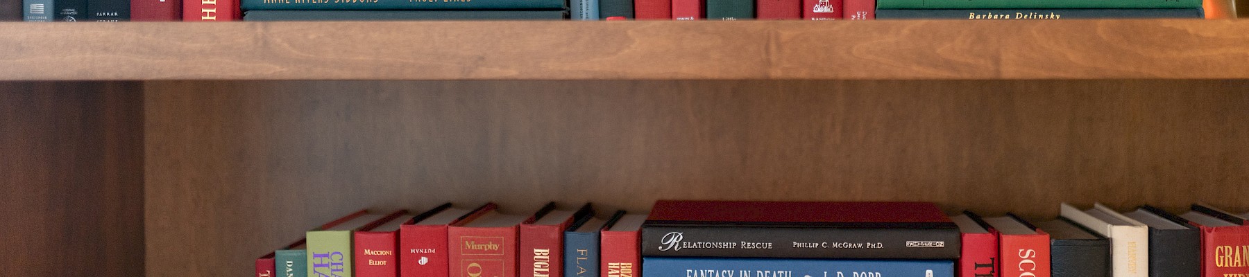 A wooden shelf filled with various books and a small white bust.