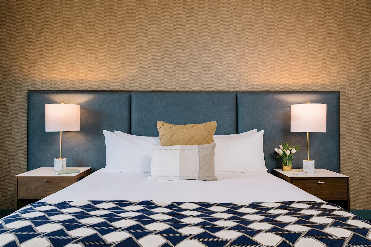 This image shows a neatly made bed with a headboard, flanked by two nightstands with lamps, and decorative items under soft lighting.