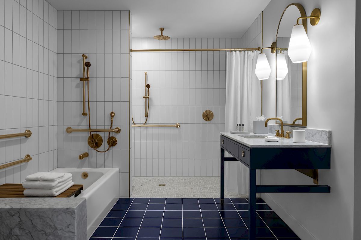 A modern bathroom with white tiles, a bathtub, a shower area, a vanity with a sink, large mirror, and gold fixtures, ending the sentence.