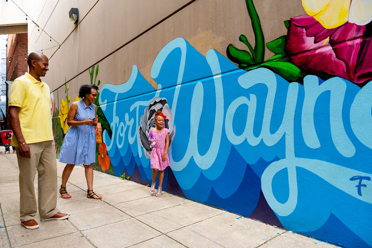 A family admires a colorful mural with the words 