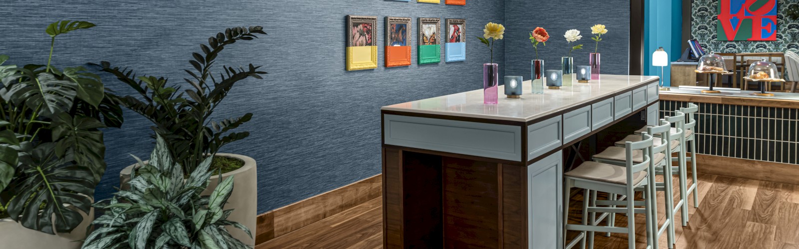 The image shows a modern room with a long table, chairs, wall art, plants, and contemporary lighting. The ambiance is cozy and stylish, ending the sentence.