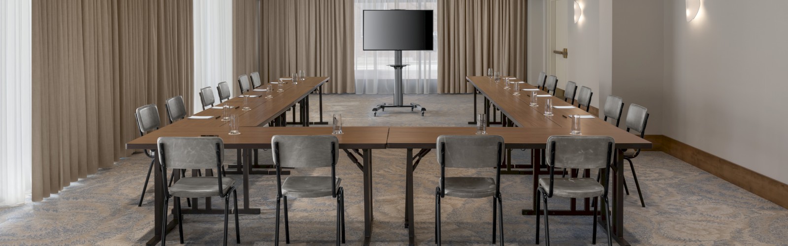 The image shows a modern conference room with U-shaped table arrangement, chairs, two ceiling lights, beige curtains, and a TV screen.