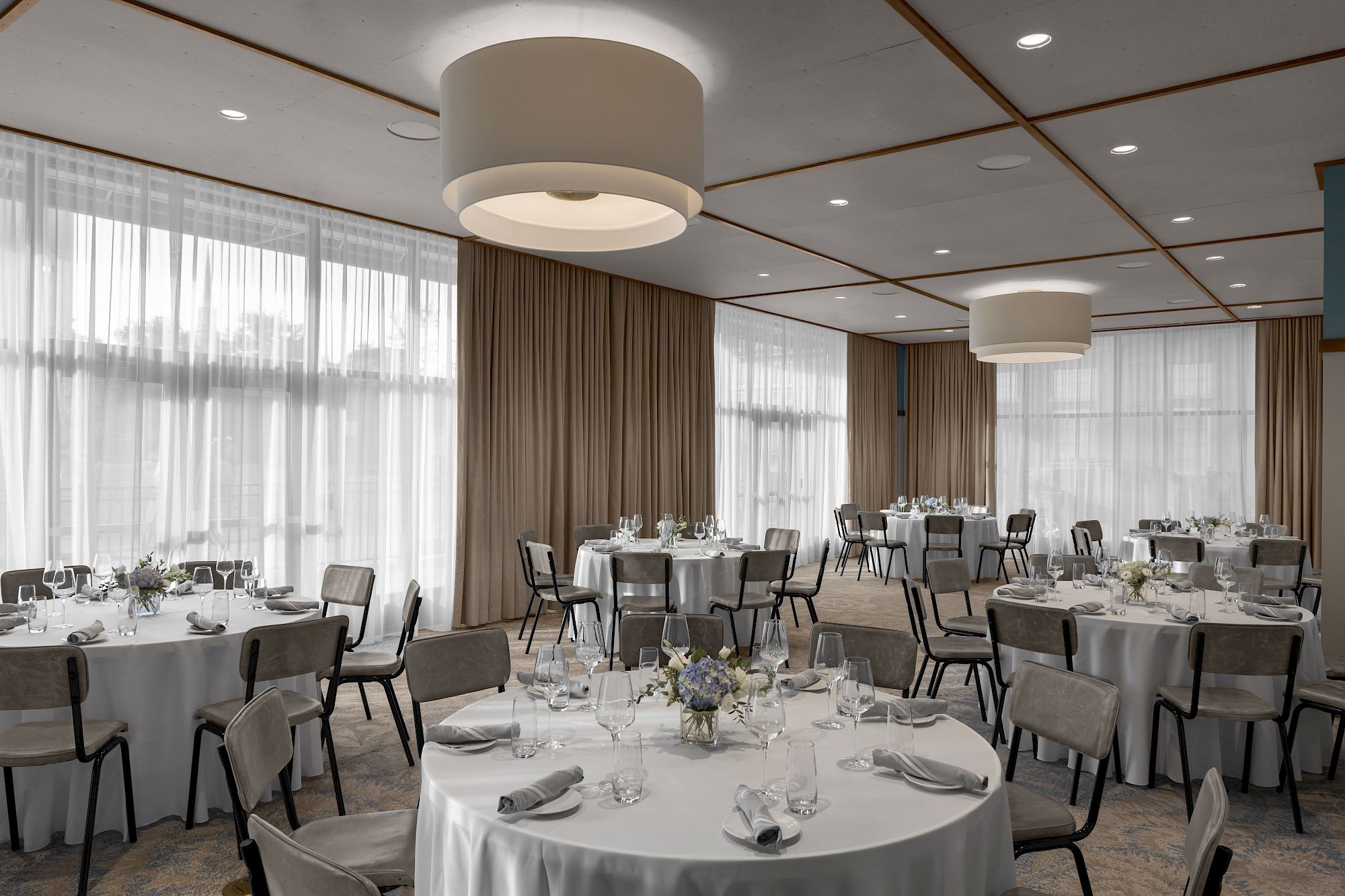 This image shows an elegantly set banquet hall with round tables, white tablecloths, and modern light fixtures, suitable for an event or wedding.