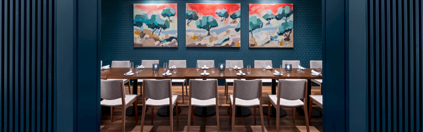 A modern dining room features a long table with chairs, stylish artwork on the walls, and a central hanging light fixture.