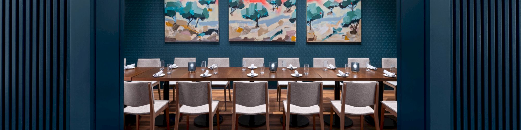 A modern dining room features a long table with chairs, stylish artwork on the walls, and a central hanging light fixture.