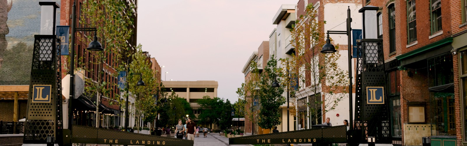 A pedestrian street flanked by brick buildings and trees, featuring an archway with 