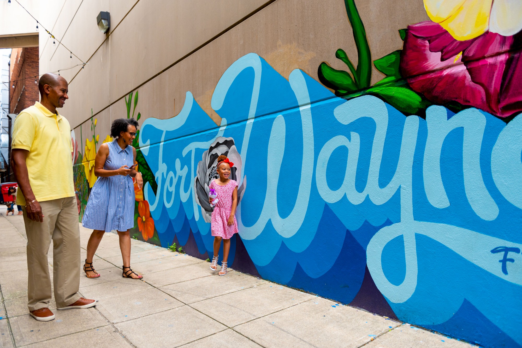 Three people admire a colorful mural that says 