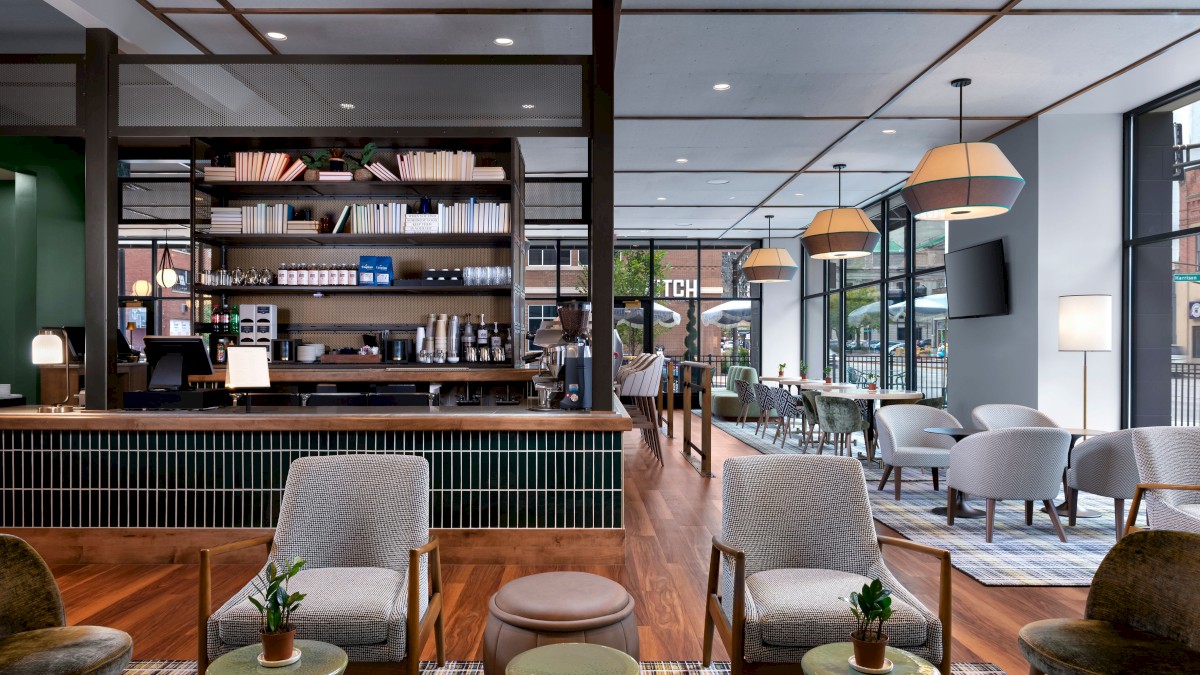 A modern café with a stylish interior, featuring a variety of seating options, a coffee bar, and large windows allowing natural light.