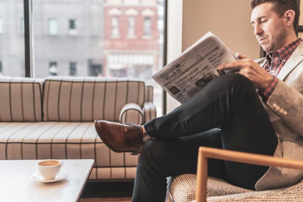 A man sits in a cozy room, reading a newspaper with a coffee cup on the table nearby.