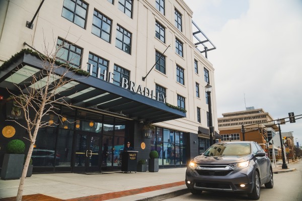 The image shows a city street with a black SUV parked in front of a hotel named 