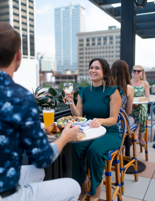 People dining on a rooftop patio with city views, enjoying drinks and conversation.