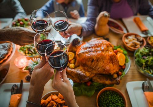 Several people clink wine glasses over a table set with a roast turkey, various side dishes, and vegetables during a festive meal, ending the sentence.