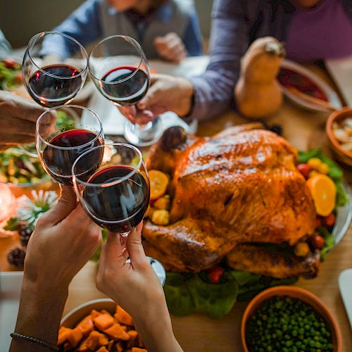 Several people clink wine glasses over a table set with a roast turkey, various side dishes, and vegetables during a festive meal, ending the sentence.