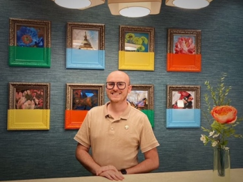 A person stands in front of a wall with eight framed images; the bottom halves of the frames are painted in different colors.