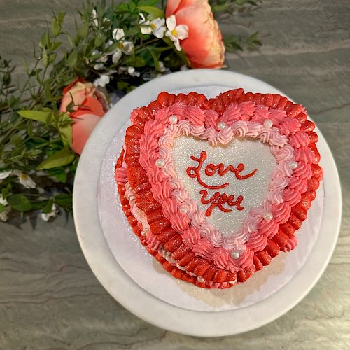 A heart-shaped cake with red and pink frosting, displaying the words 