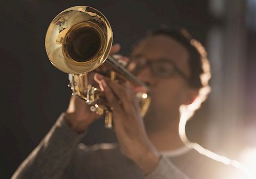 A person playing a brass trumpet with blurred background. The image focuses primarily on the instrument rather than the person.