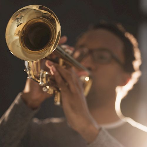 A person playing a brass trumpet with blurred background. The image focuses primarily on the instrument rather than the person.