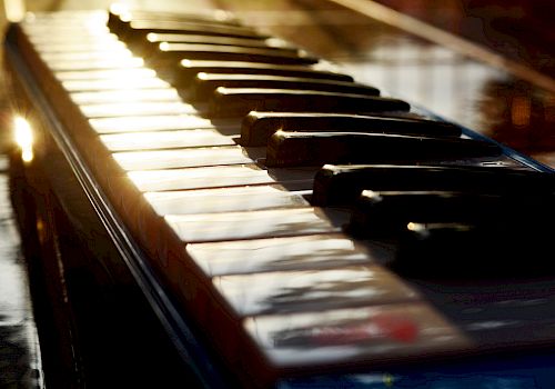 This image shows the keys of a piano with sunlight reflecting off them, creating a warm and inviting atmosphere.