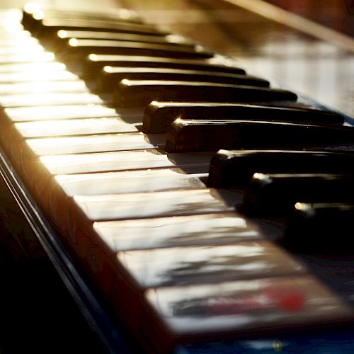 This image shows the keys of a piano with sunlight reflecting off them, creating a warm and inviting atmosphere.