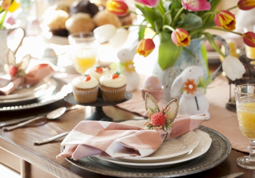 A beautifully set table with tulips, cupcakes, and decorated napkins. The table has orange juice and utensils ready for a meal.