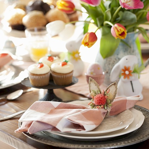 A beautifully set table with tulips, cupcakes, and decorated napkins. The table has orange juice and utensils ready for a meal.