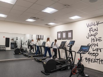 Two people are using treadmills in a well-lit gym with motivational words on the wall: 