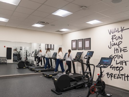 Two people are using treadmills in a well-lit gym with motivational words on the wall: 