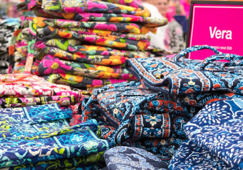 Stacks of colorful, patterned bags are displayed on a table with a sign that reads 