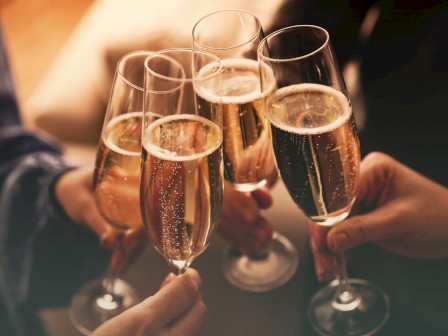 Several hands holding champagne glasses in a toast, with bubbles rising in the glasses, indicating a celebratory moment.