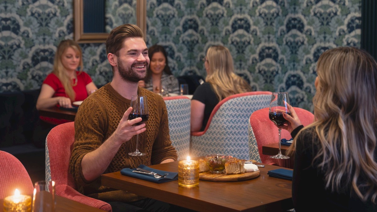 A couple dining in a cozy restaurant, sharing a moment over wine and appetizers, with other patrons dining in the background.