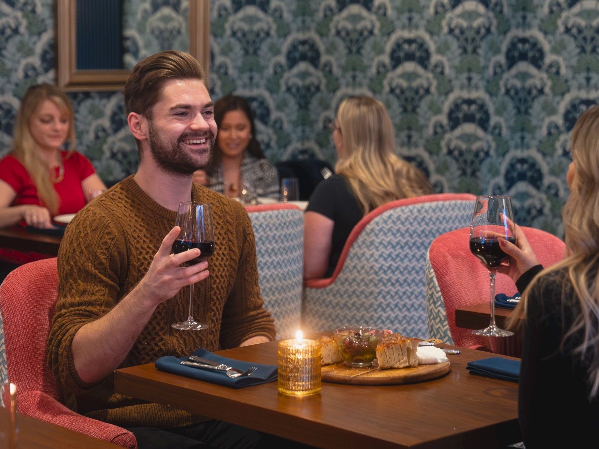 A couple dining in a cozy restaurant, sharing a moment over wine and appetizers, with other patrons dining in the background.