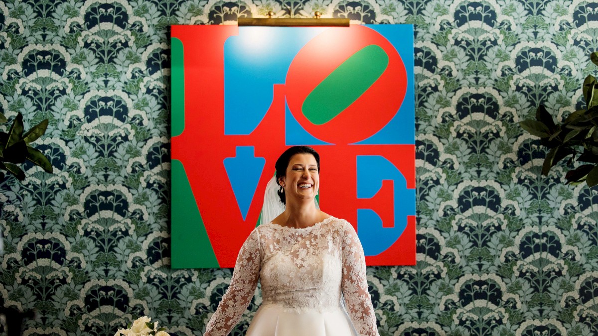 A bride in a white wedding dress stands smiling in front of a colorful 