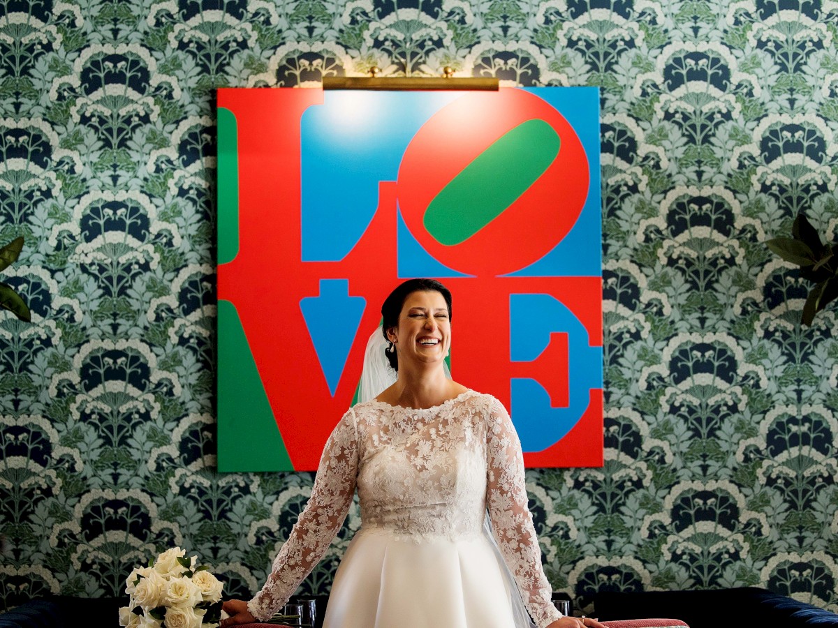 A bride in a white wedding dress stands smiling in front of a colorful 