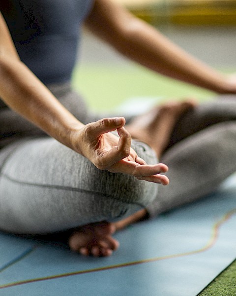 A person is sitting cross-legged on a yoga mat, meditating with their hands in a mudra pose. They are dressed in athletic wear.