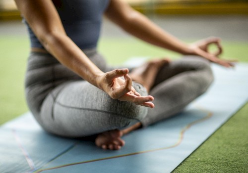 A person is sitting cross-legged on a yoga mat, meditating with their hands in a mudra pose. They are dressed in athletic wear.