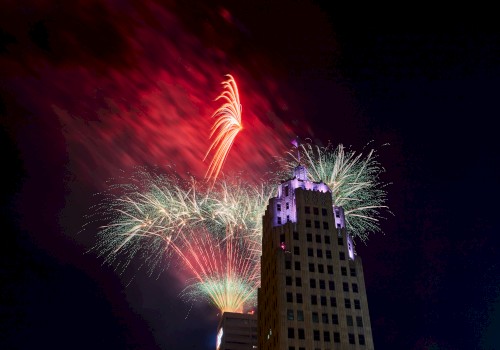 A night scene with colorful fireworks exploding in the sky behind a tall, illuminated building.