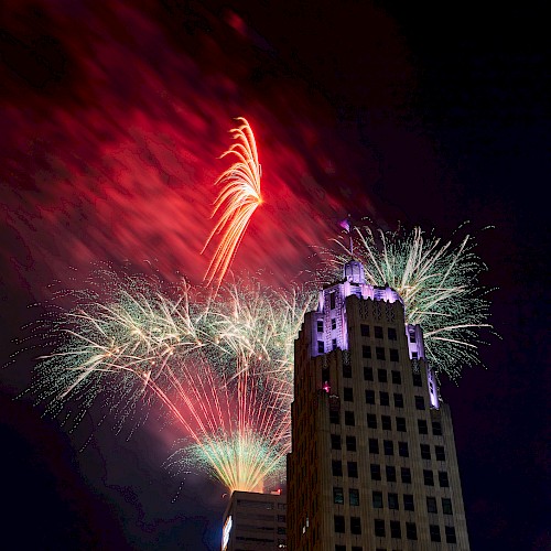 A night scene with colorful fireworks exploding in the sky behind a tall, illuminated building.