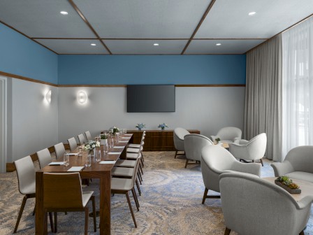 A modern conference room with a long table, chairs, lounge seating, a TV, and decor on the table and walls, under soft lighting.