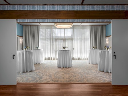 An elegantly set up room with round, white-clothed cocktail tables, floral arrangements, and curtains, with soft lighting creating a refined ambiance.