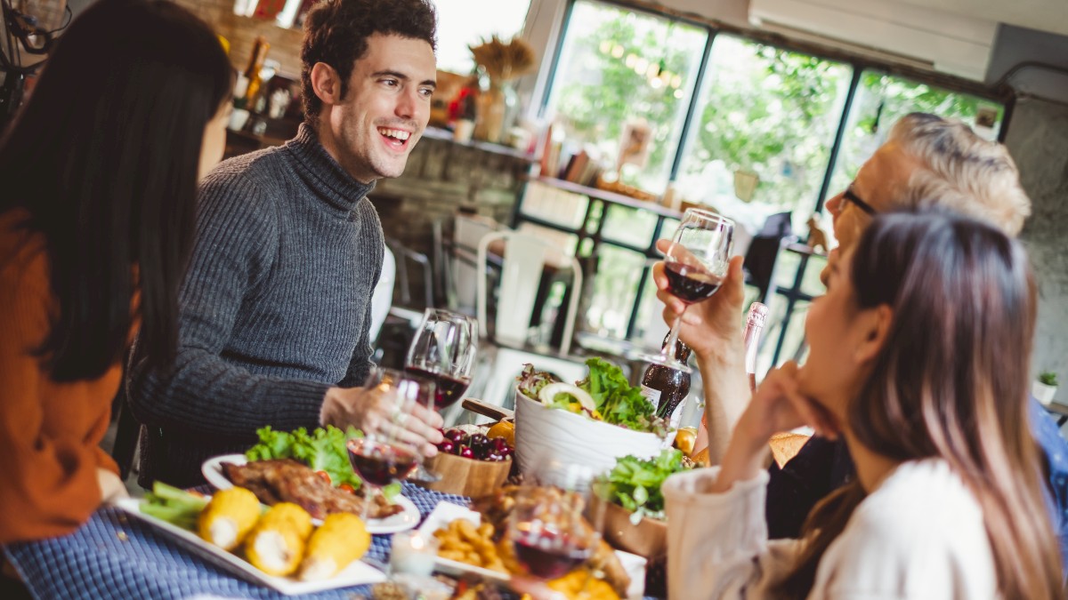 A group of people are enjoying a meal together, holding glasses of wine in a cozy setting.