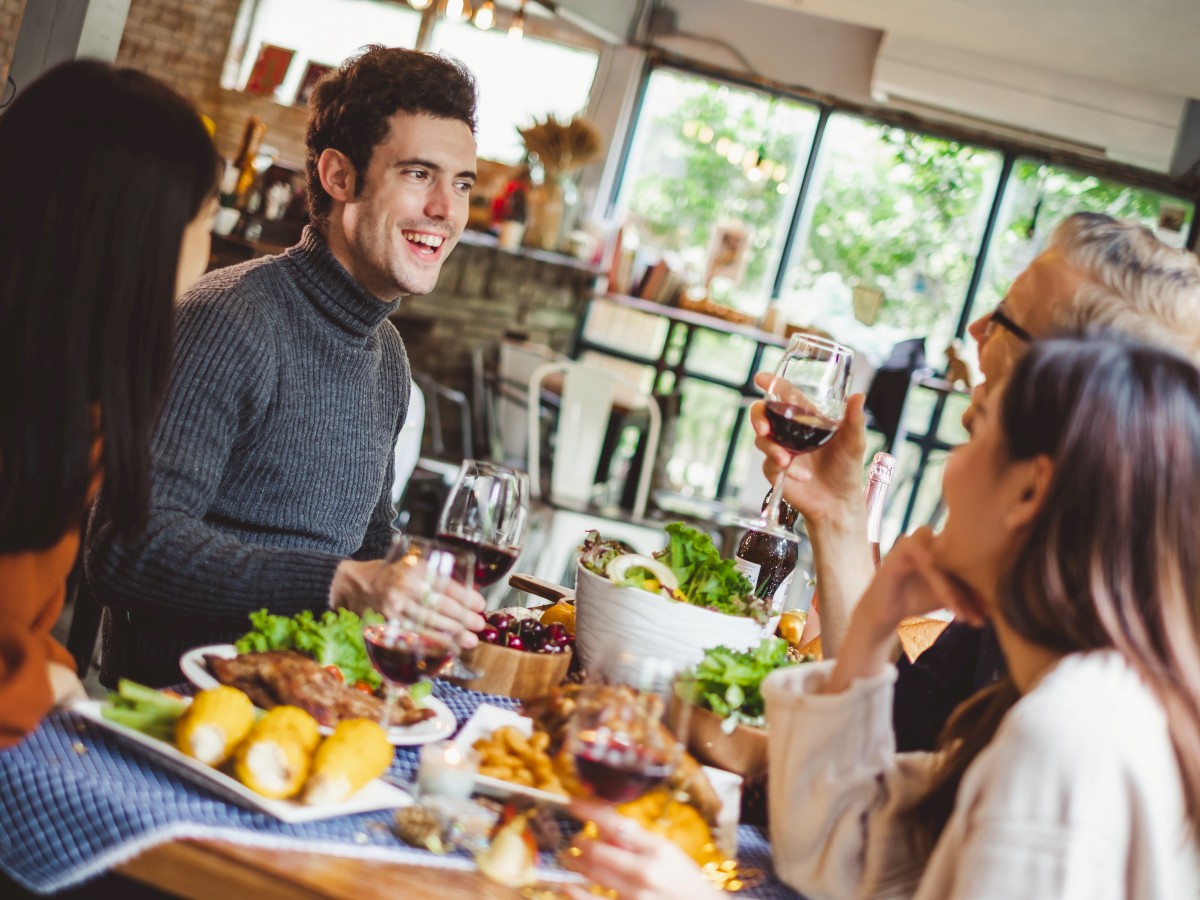 A group of people are enjoying a meal together, holding glasses of wine in a cozy setting.