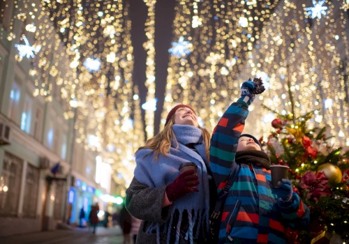 Two people enjoying festive street decorations with warm drinks, surrounded by lights and holiday atmosphere, looking up joyfully.