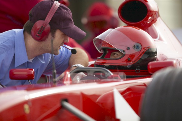 A race car driver talks with a team member wearing a headset, likely preparing for a race.