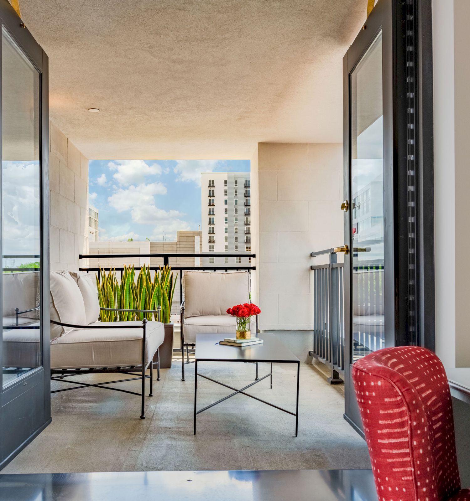 A modern interior opens to a balcony with a seating area, a small table holding flowers, and a city view in the background, ending the sentence.