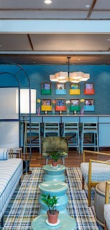 A modern lounge with striped sofas, colorful artwork, pendant lights, and a table with high chairs against a blue wall.