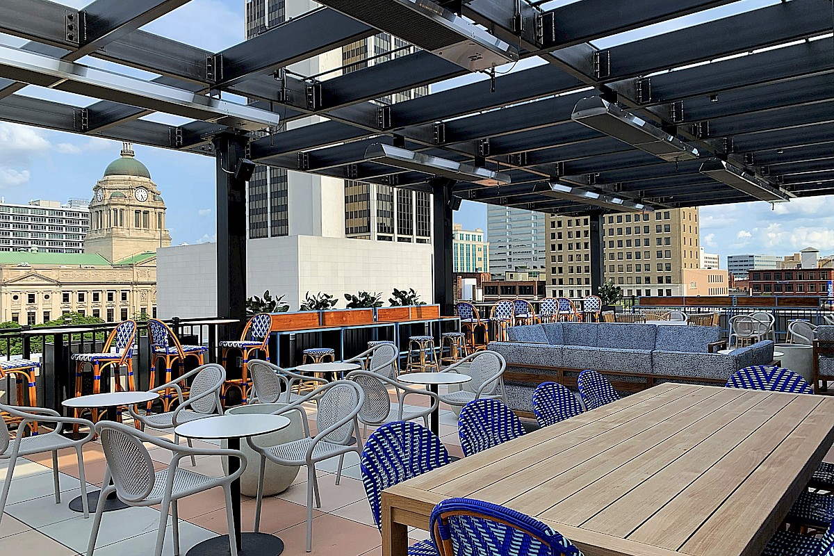 Rooftop patio with tables, chairs, and sofas, overlooking a cityscape with a historic dome building in the background.