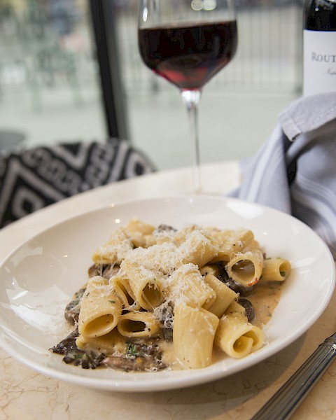 A plate of pasta with sauce and cheese, a glass of red wine, and a wine bottle on a table.