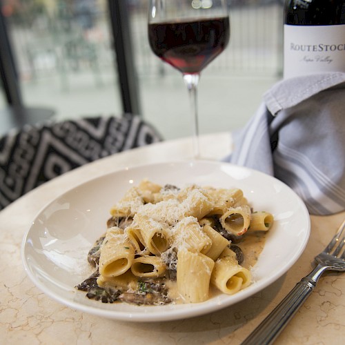 A plate of pasta with sauce and cheese, a glass of red wine, and a wine bottle on a table.